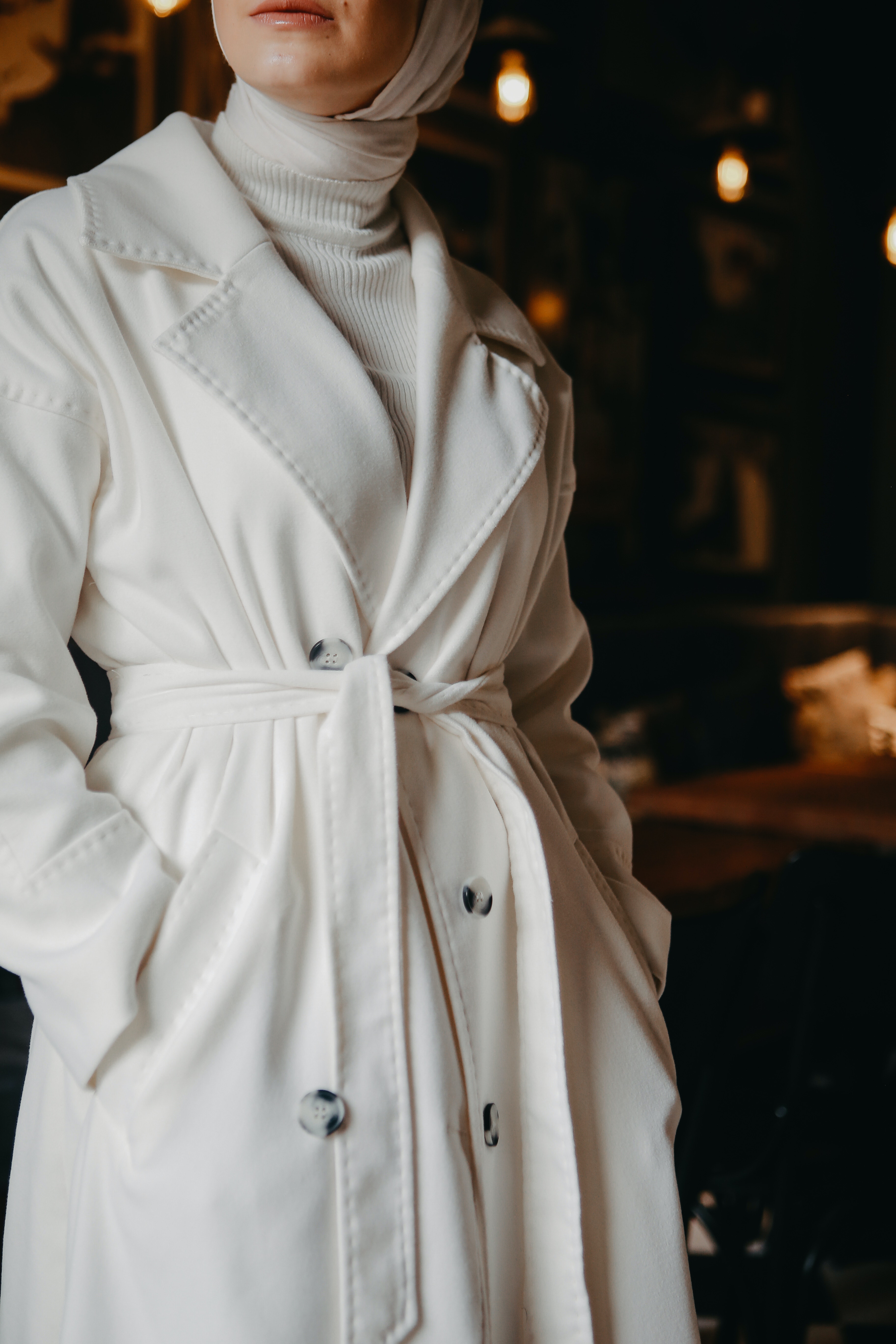 Model wears all white ensemble with a belted coat and head wrap